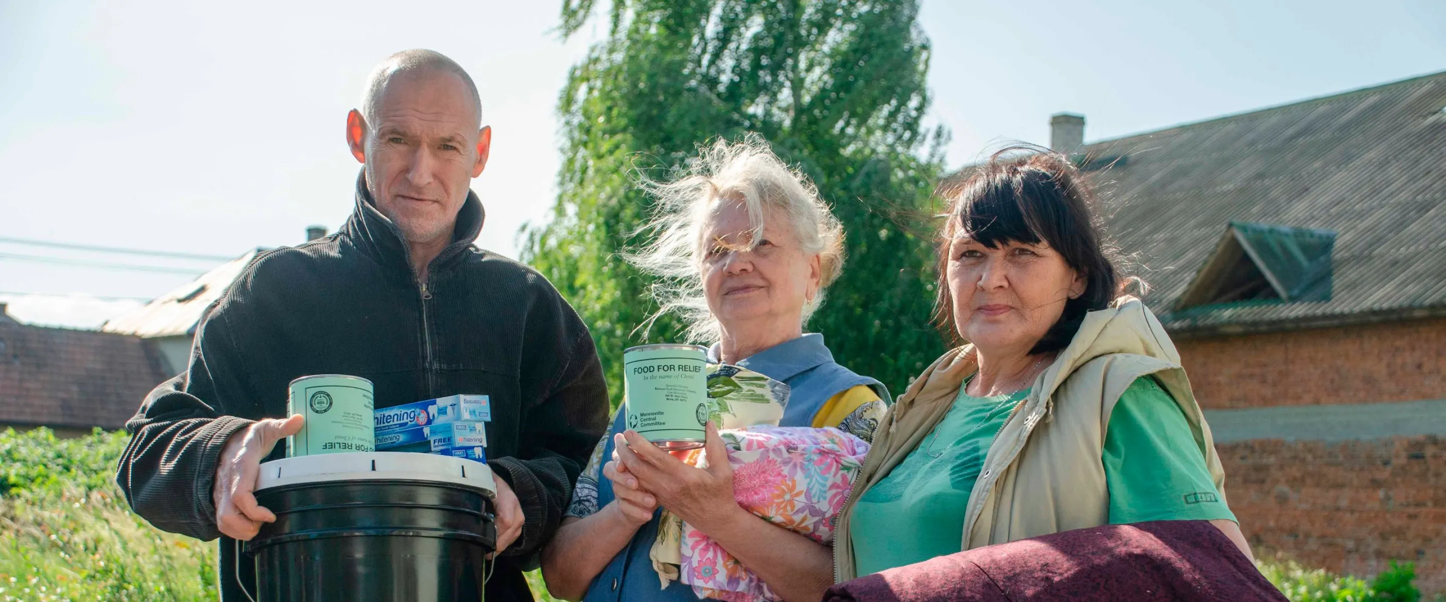 A man and two women hold up relief kit items and quilts