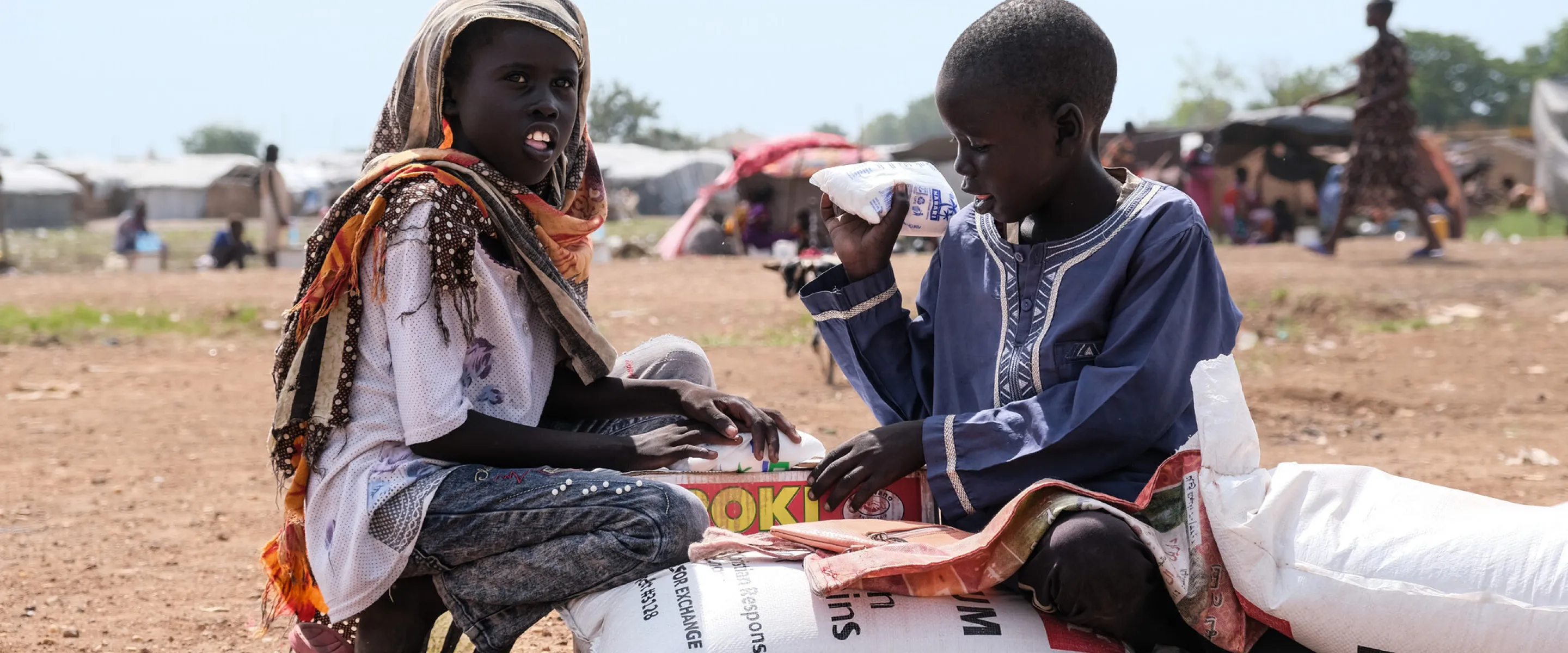 Zero Mawang Juch (left) and Sudan Koang Ruei at the distribution site with a portion of food supplies. Each bag of sorghum is about 15kgs, so it is heavy for program participants to carry on their he