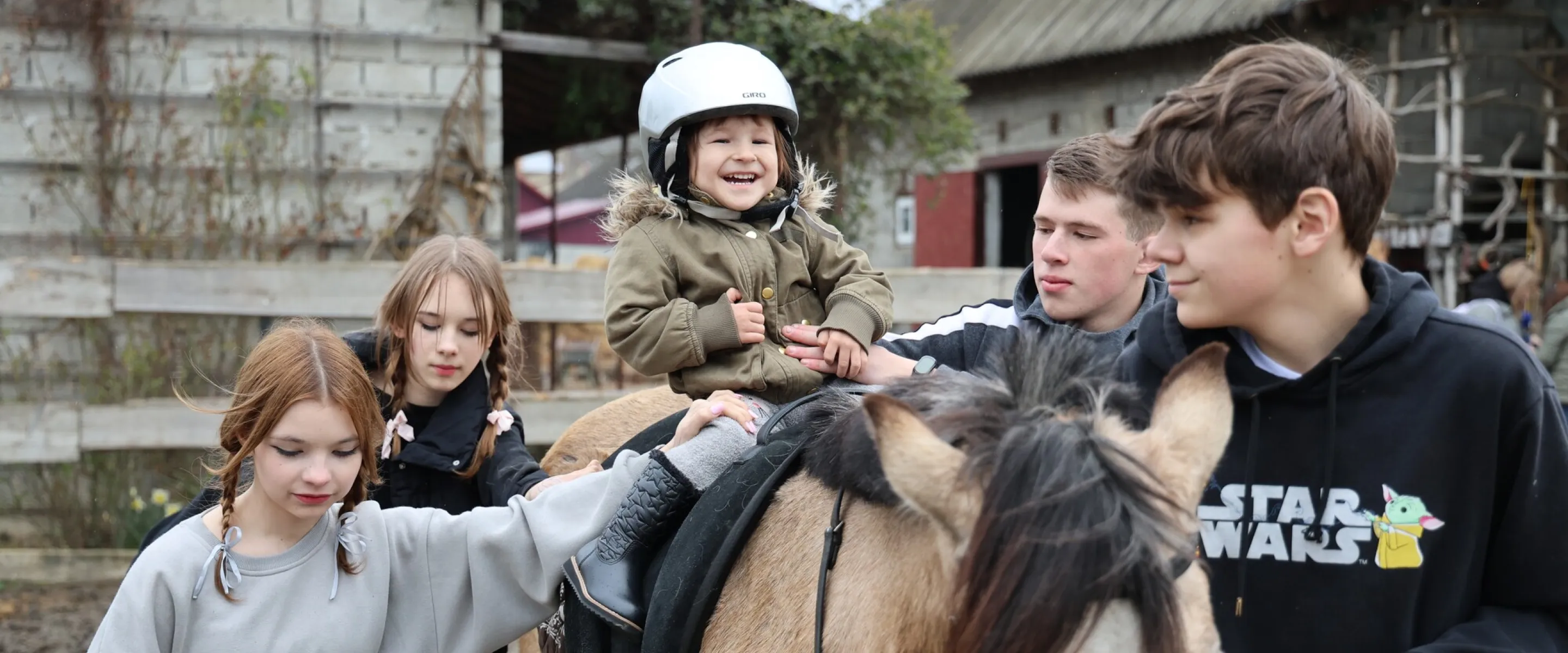 Three-year-old Vasylisa* sits calmly with assistance from volunteers during therapeutic horse riding for children who are displaced and affected by war.MCC, with partner Association of Mennonite B