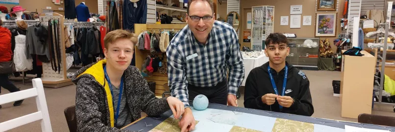 Two youth and an adult pose for the camera while sitting around a comforter in a thrift shop.