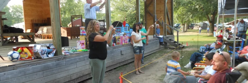 An auctioneer stands on an outdoor stage. Two women are down below displaying toys that are for auction.