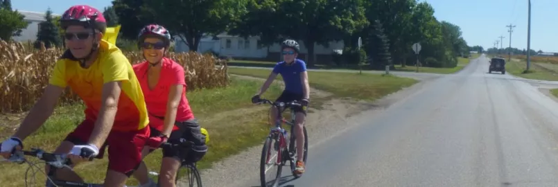 Two people ride a tandem bike while another cyclist follows behind them.