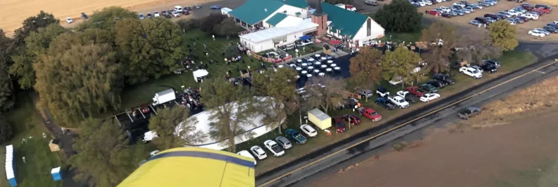 An overview view of a church building during an event. There are a lot of cars parked around the church. The photo was taken out the window of a yellow airplane.