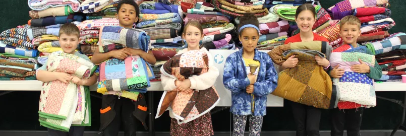 children standing and holding colorful comforters