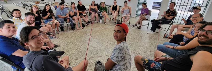 Young people sitting in a circle connected by web of string.