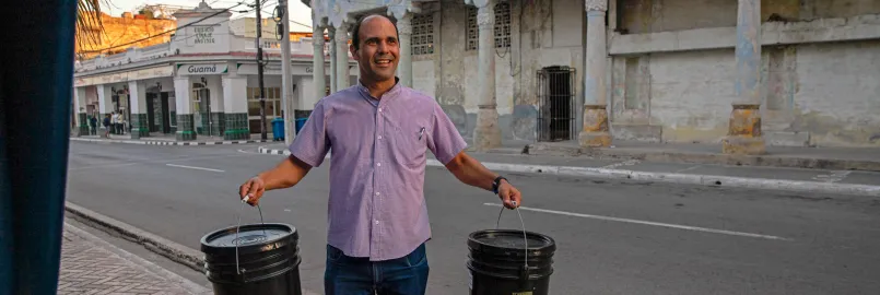 A man from Cuba holds two relief kits on a sidewalk. 