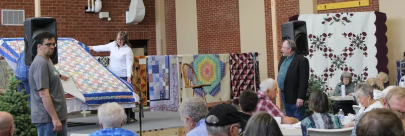  People sitting in audience for quilt auction.