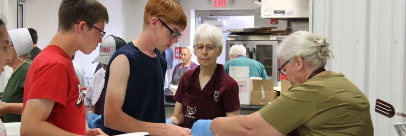 woman serving pancakes to two boys