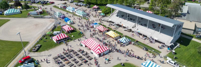 A photo from several feet in the air which shows several tents, a grandstand, and visitors on the ground.