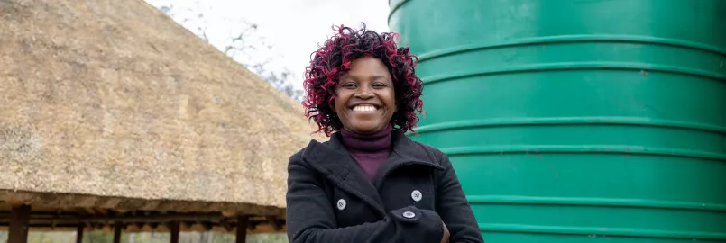 Woman stands beside water tank, smiling.