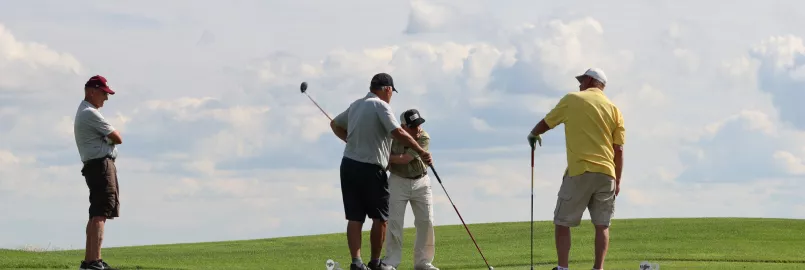 four golfers on a green in front of a blue sky