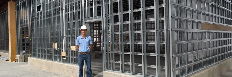 man in hard hat stands in front of a wall of steel studs under construction