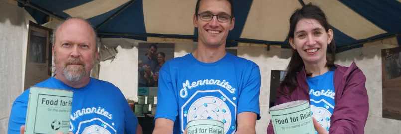 Standing outside a tent, three people wearing identical blue shirts each hold out a can that reads "Food for Relief" to the camera.