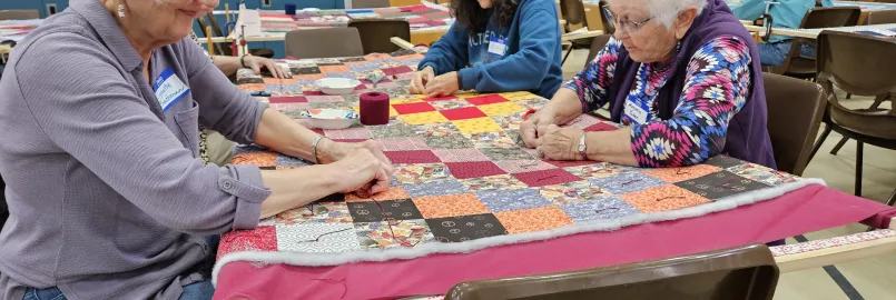 A group of people knot a comforter.