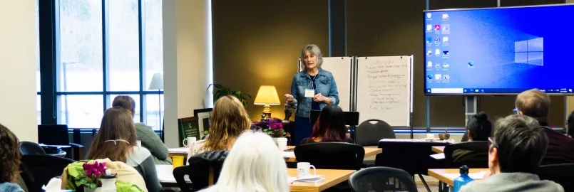 A woman presents to a group of people at the front of a room.