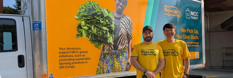 Two men in yellow stand in front of an MCC Thrift truck that is also yellow with images on it.