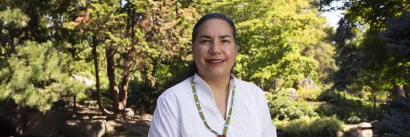 A woman wearing a white shirt sits in front of a lush green landscape.