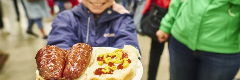 A girl holding a plate of farmers sausage on a bun