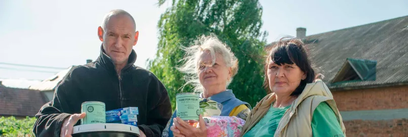 A man and two women hold up relief kit items and quilts