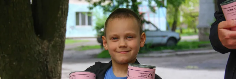 A boy* holds cans of meat he and his mother (not pictured) received from volunteers with MCC partner Association of Mennonite Brethren Churches of Ukraine (AMBCU). The canned meat was part of a distri