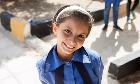 A girl in a blue school uniform smiles at the camera