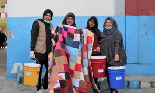 Four women stand together and pose with a comforter and three five-gallon buckets.