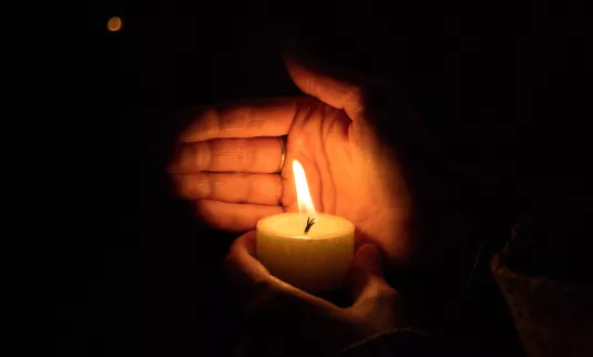 A hand cupping a candle's flame.