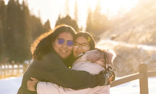 Two people hugging with snow in the background.