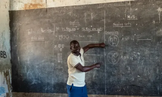 Teacher at a large chalk board in Uganda.