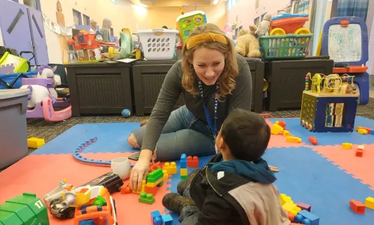 A smiling person sits on the floor with a small child.
