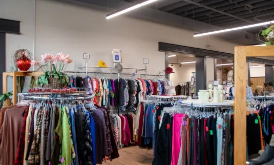 The photograph shows a clothing store interior with racks of garments, shelves with items, and decorative plants.
