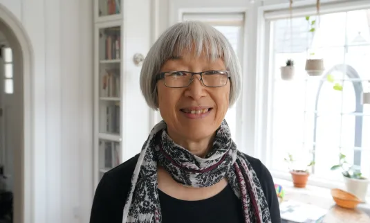 A portrait of an older woman with short grey hair, glasses, wearing a scarf