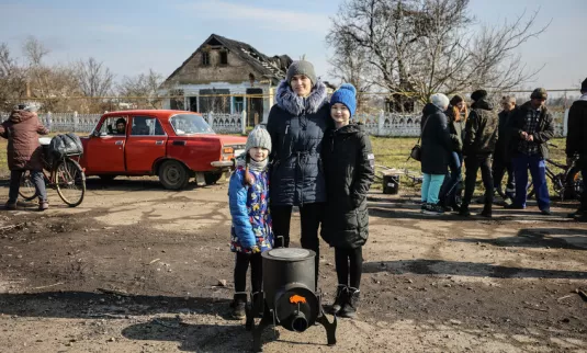 This family* in a village recovered from Russian military control in Ukraine's Kherson region stand with the wood stove they received from MCC partner Charitable Foundation Uman Help Center (Uman Help