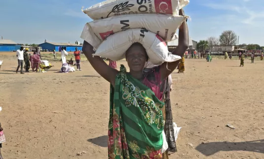 Nyachar Kueth Kang carries bags of sorghum she received during a May 2021 distribution of food assistance in Rubkona county, South Sudan, by the relief and development agency of the Episcopal Church o