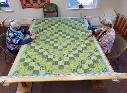 Two women stitching a green quilt