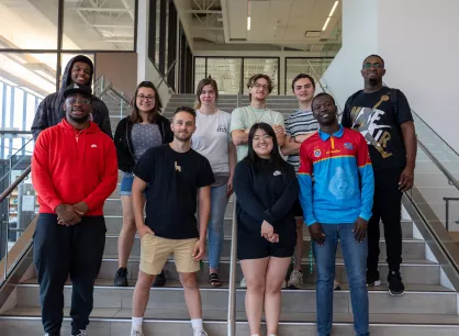 RS129108_MicrosoftTeams-image (3)-hpr.jpg Ten young adults stand together for a group photo on a set of stairs.