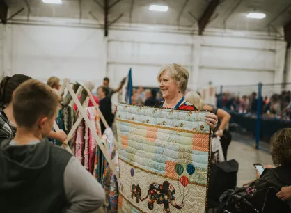 Volunteer holding up a quilt for customers.
