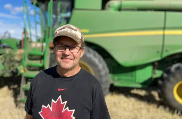 A farmer from Alberta with the Grow Hope project stands in front of his equipment in a field. 