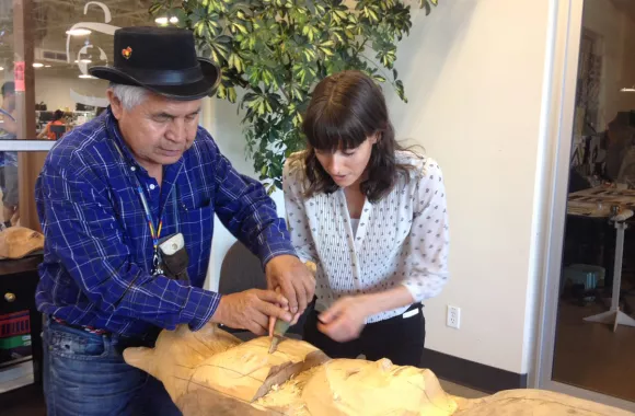 A man and a woman work together on carving a log