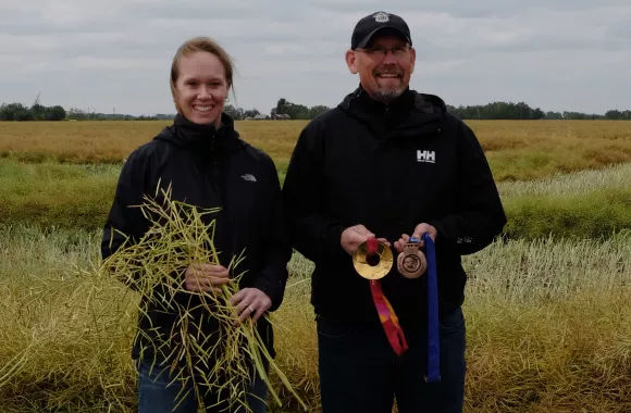 Woman in a field holding grain with a farmer holding olympic medals