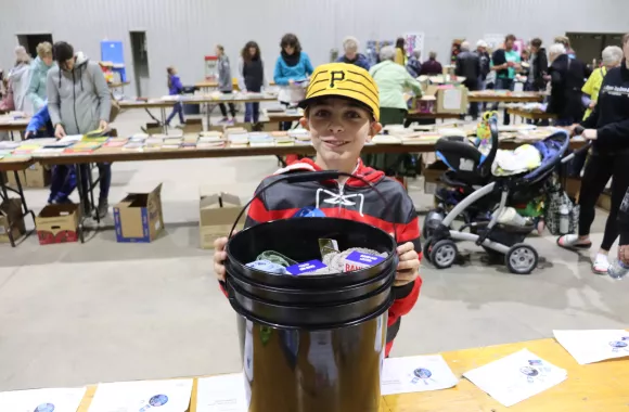 A boy in a ball cap stands behind a five-gallon bucket packed with supplies