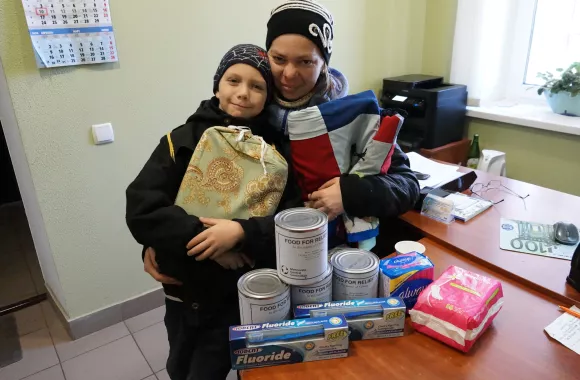 A mother with her arm around her child pose with humanitarian aid items.