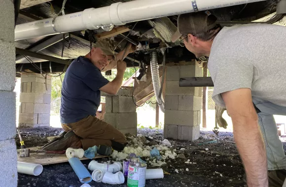 Volunteers serving with MCC's Sharing With Appalachian People (SWAP) Greg Breslin, left, and Dale Esbin work together to repair plumbing under the mobile home of Brenda Kelsor, a homeowner near Northfork, West Virginia. Previously Brenda's floors were unsafe due to plumbing leaks over time, and bathroom fixtures were not functional.