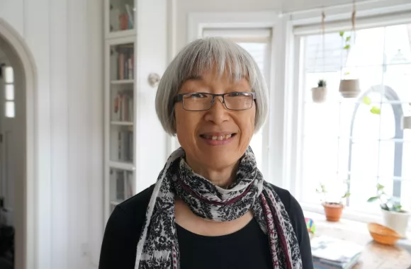 A portrait of an older woman with short grey hair, glasses, wearing a scarf