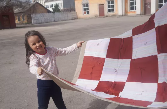 A young girl holds the edge of a red and white comforter