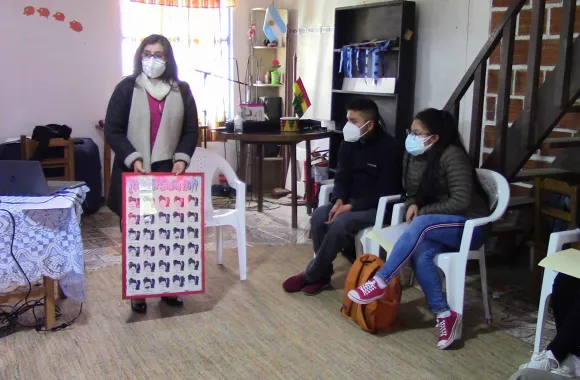 A woman in a face mask holds a poster and speaks to a group of people who are sitting.
