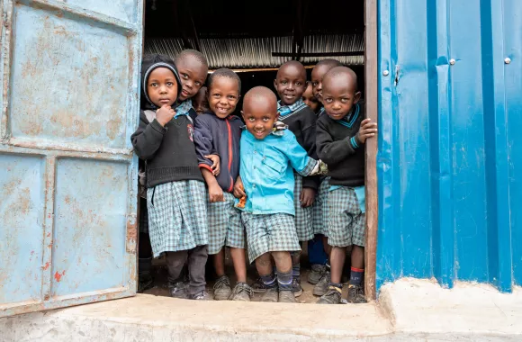 A group of Kenyan school children in uniforms stand in the doorway of their school