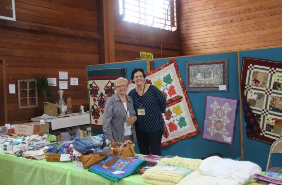 Two women stand in a booth selling quilts