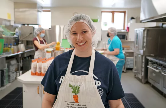 Smiling woman wearing an apron in a commercial kitchen.