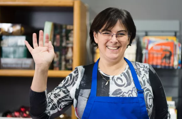 A volunteer smiling and waving in an MCC Thrift shop